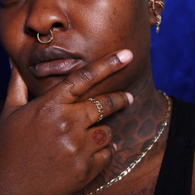 A model touching their chin wearing various Automic Gold rings, piercings, and necklaces