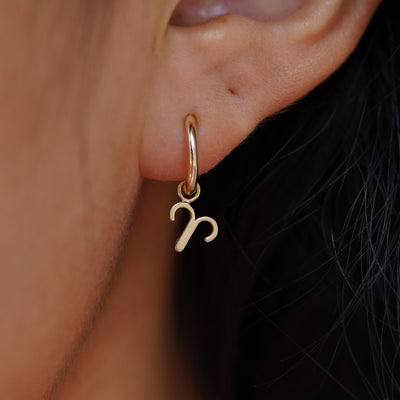 Close up view of a model's ear wearing a yellow gold Ares Horoscope Charm on a Curvy Huggie Hoop